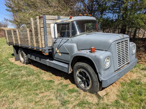 An old gray pick up truck with a wooden railing around the truck bed.